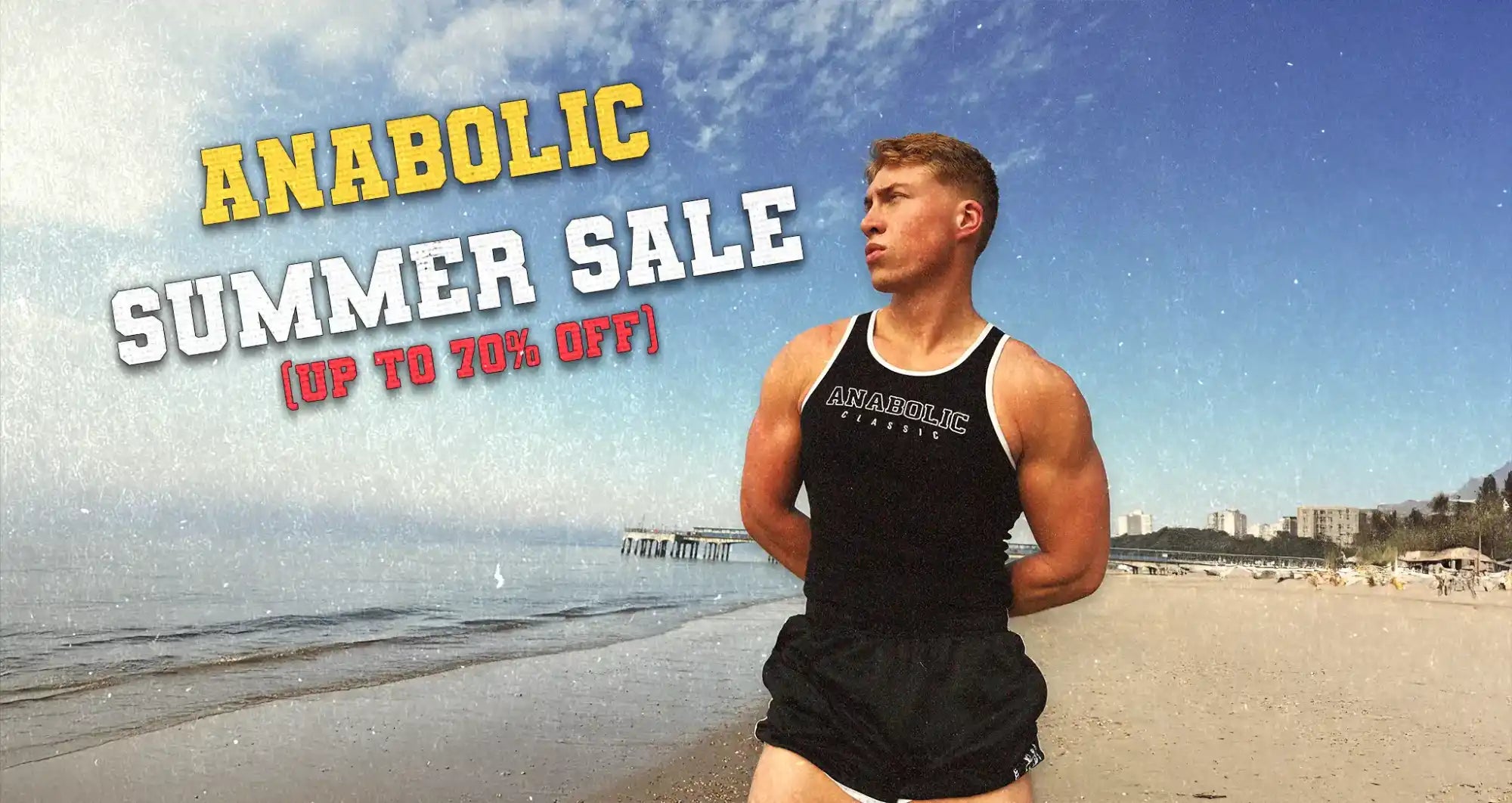 Muscular man in a black tank top and shorts on a beach.